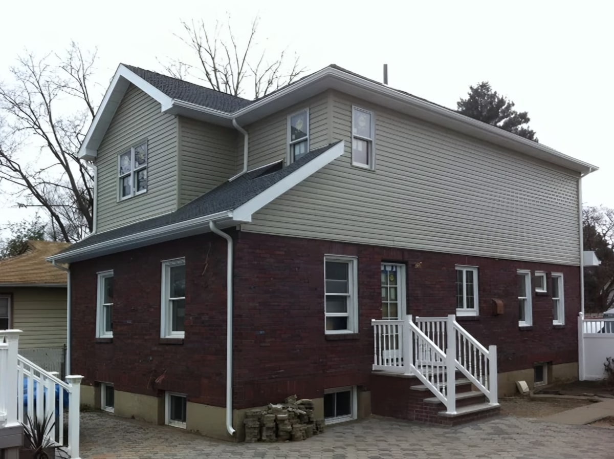 Brick and green vinyl siding house with new roof and white railings